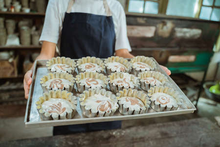 close up of a womans hand carrying a baking sheet filled with several small cake moldsの写真素材
