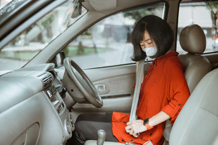 Woman in protective mask driving a car on road. Safe traveling fasten seat beltの写真素材