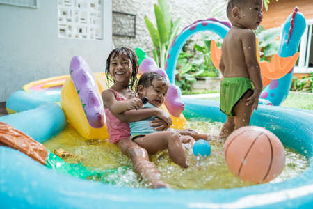 big sister smiles hugging younger sister while playing together in rubber pool portableの写真素材