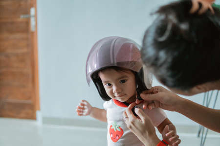 little baby wears a motorcycle helmet when fastened by its motherの写真素材