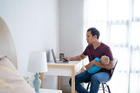father working from home while holding his infant babyの写真素材