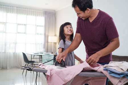 Father with little daughter ironing kids clothes at home.Domestic conceptの写真素材