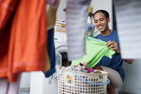 househusband putting dirty clothes one by one into washing machine doing laundryの写真素材