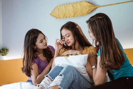 Women talking and consoling their sad friend in the bedroomの写真素材