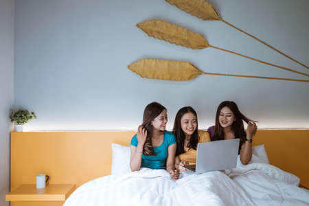 girls using laptop together on a bed in bedroomの写真素材