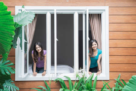 two beautiful twin sister at home standing by the windowの写真素材