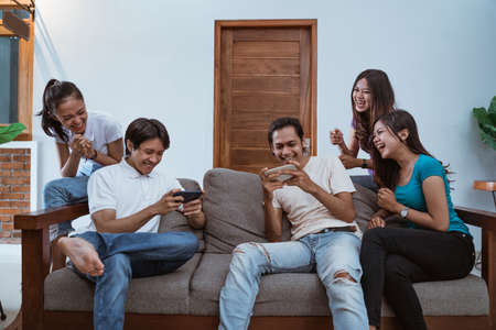 excited friends together playing games with smartphones at homeの写真素材