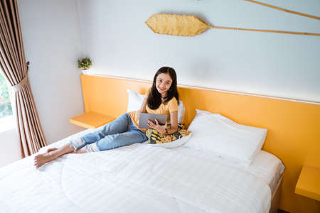 woman lying in bed with digital tablet touching with finger in morning sunlightの写真素材