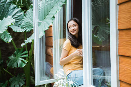 beautiful woman drinking coffee in the morning by the window. view from outside.の写真素材