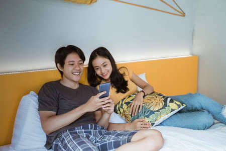 couple using smart phone and smiling while spending time in bed at homeの写真素材