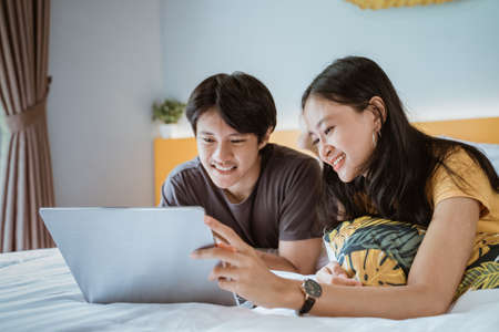couple relaxing on bed using the laptop at home in the bedroomの写真素材