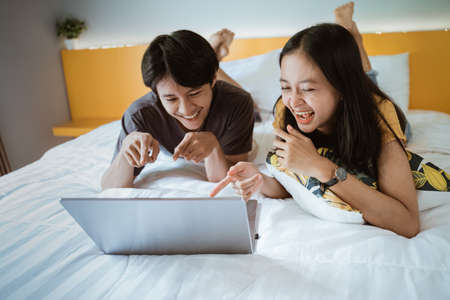 couple relaxing on bed using the laptop at home in the bedroomの写真素材