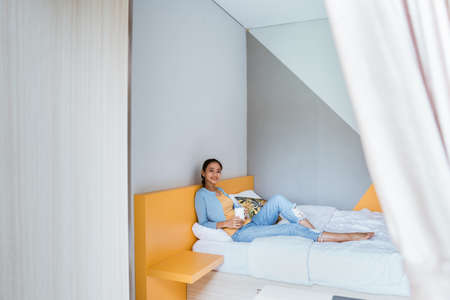 asian woman having coffee in cozy bedroom. Morning rituals.の写真素材