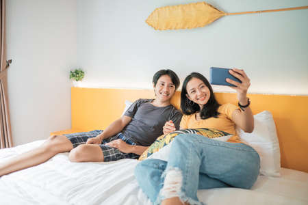 couple using smart phone and smiling while spending time in bed at homeの写真素材