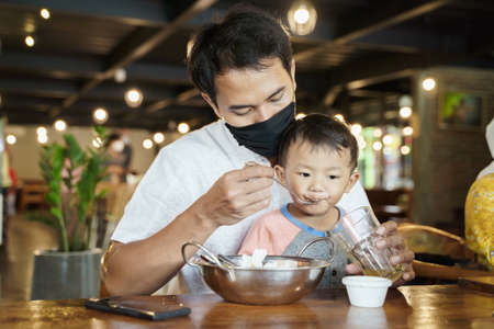 father feeding his son at restaurantの写真素材