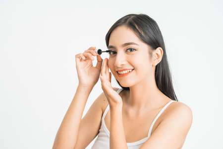 mixed race asian woman putting mascara on eyelashes on white backgroundの写真素材