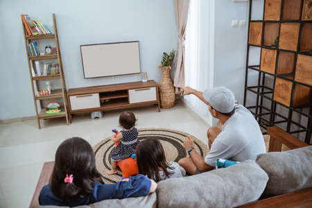Family Sitting On Sofa At Home Watching TV Togetherの写真素材