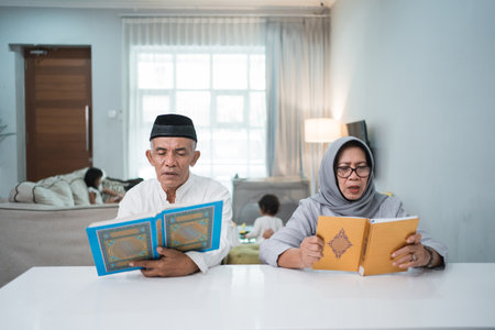 Asian Muslim senior man teaching wife reading Koran or Quran in living roomの写真素材