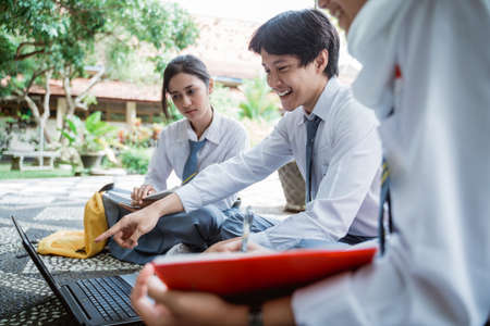 a male high school student in Indonesia smiles with a finger pointing at a laptop screen while studying a groupの写真素材