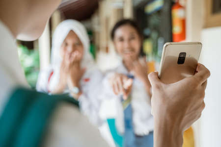 selective focus picture of a smartphone being held by a student is shown to two female high school studentsの写真素材