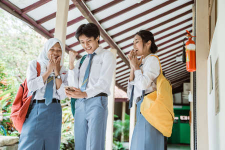 Three high school students look at the screen using one smartphone to see the announcement of graduationの写真素材