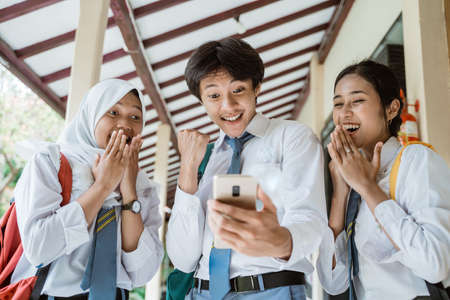close up of three high school students look at the screen using one smartphone to see the announcement of graduationの写真素材