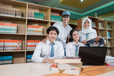 four high school students smiling looking at the camera while studying together with a pile of books and a laptop on a table with copyspaceの写真素材