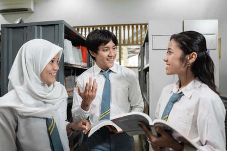 three high school students in uniform chatting while reading booksの写真素材
