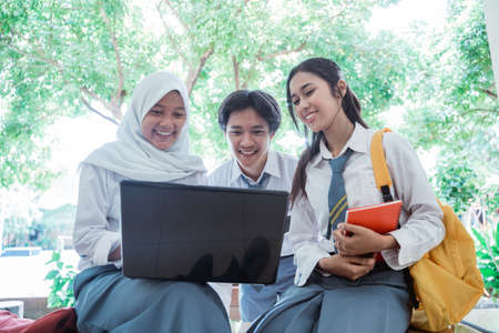 front view of high school students standing with a laptop computer, carrying books, and wearing a bagの写真素材