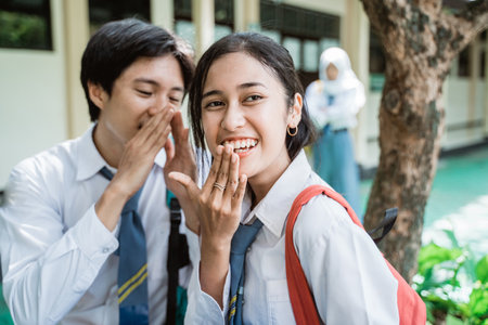 a boy whispered to smile girl in high school uniform when sitting in the school garden with female friend standの写真素材