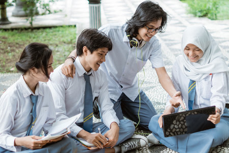 four teens in high school uniform use a laptop doing group assignment sittingの写真素材