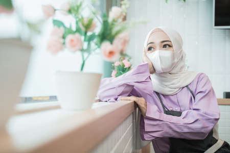 unhappy young muslim woman wear mask while looking out the windowの写真素材
