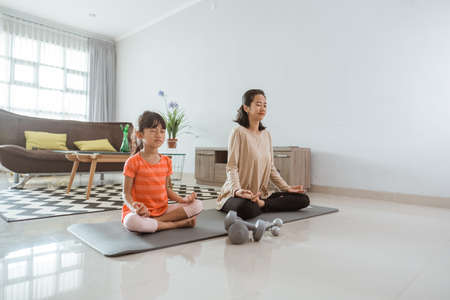 mother doing yoga exercise at at home with her daughter togetherの写真素材