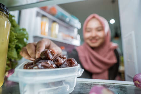 muslim asian woman eating dates fruit in front of the fridgeの写真素材