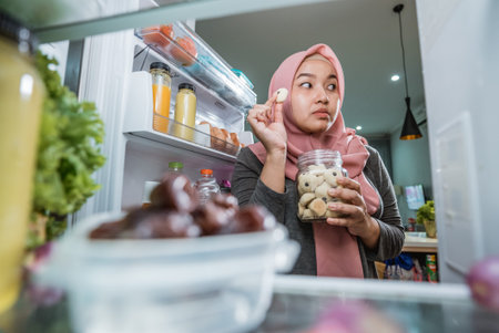 young muslim woman fail her diet by eating sweets snack in the fridgeの写真素材