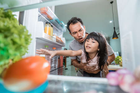 portrait of asian father preventing her daughter to take some food inside the fridgeの写真素材