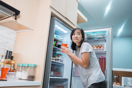 asian woman cheat diet and drinking sweet drink taking from the refrigeratorの写真素材