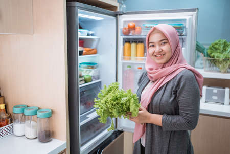 portrait of asian muslim woman open fridge door and getting ready to cook for dinnerの写真素材