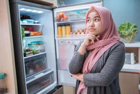 muslim asian woman thinking while open the refrigerator door before cooking in the kitchenの写真素材