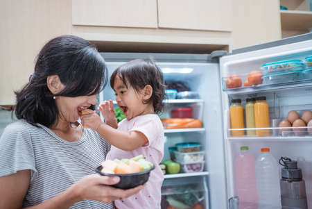 mother carrying her toddler baby and eat fruit together in the kitchenの写真素材