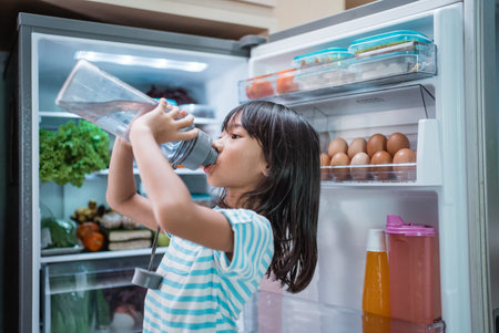 thirsty happy young asian girl open fridge door drinking a bottle of water