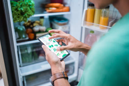 close up of hand ordering groceries online via mobile phone apps with open fridge backgroundの写真素材