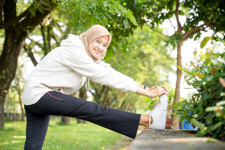 attractive asian muslim woman stretching her leg during outdoor sport aloneの写真素材