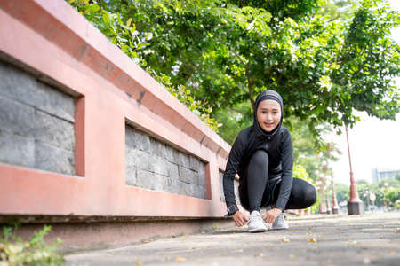 A pretty muslim woman athlete tying her shoes before running outdoorの写真素材