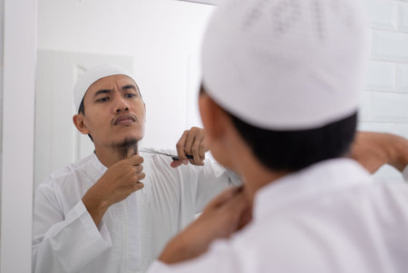 muslim asian man unsure to shave off his beard using scissor