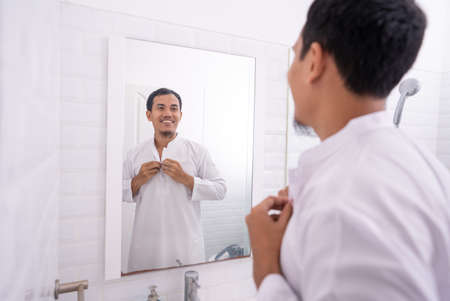 muslim asian man looking at mirror and get dressed before going to the mosqueの写真素材