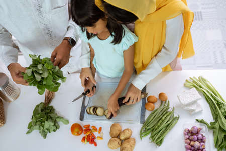 beautiful muslim asian family cooking for iftar dinner together at home. couple with kid having fun making food in the kitchenの写真素材