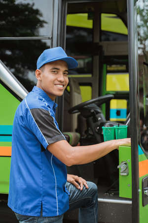 a bus driver in a uniform and a cap smiled at the camera as he stepped into the bus doorの写真素材