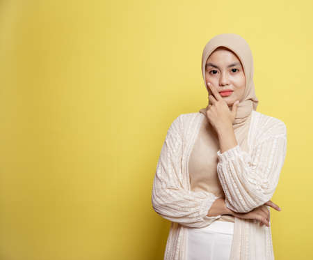woman wearing hijab smiling while pose holding her jaw looking at the camera isolated on a yellow backgroundの写真素材