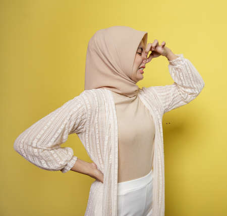 young woman wearing hijab with a smelling odor expression holding a nose isolated on yellow backgroundの写真素材